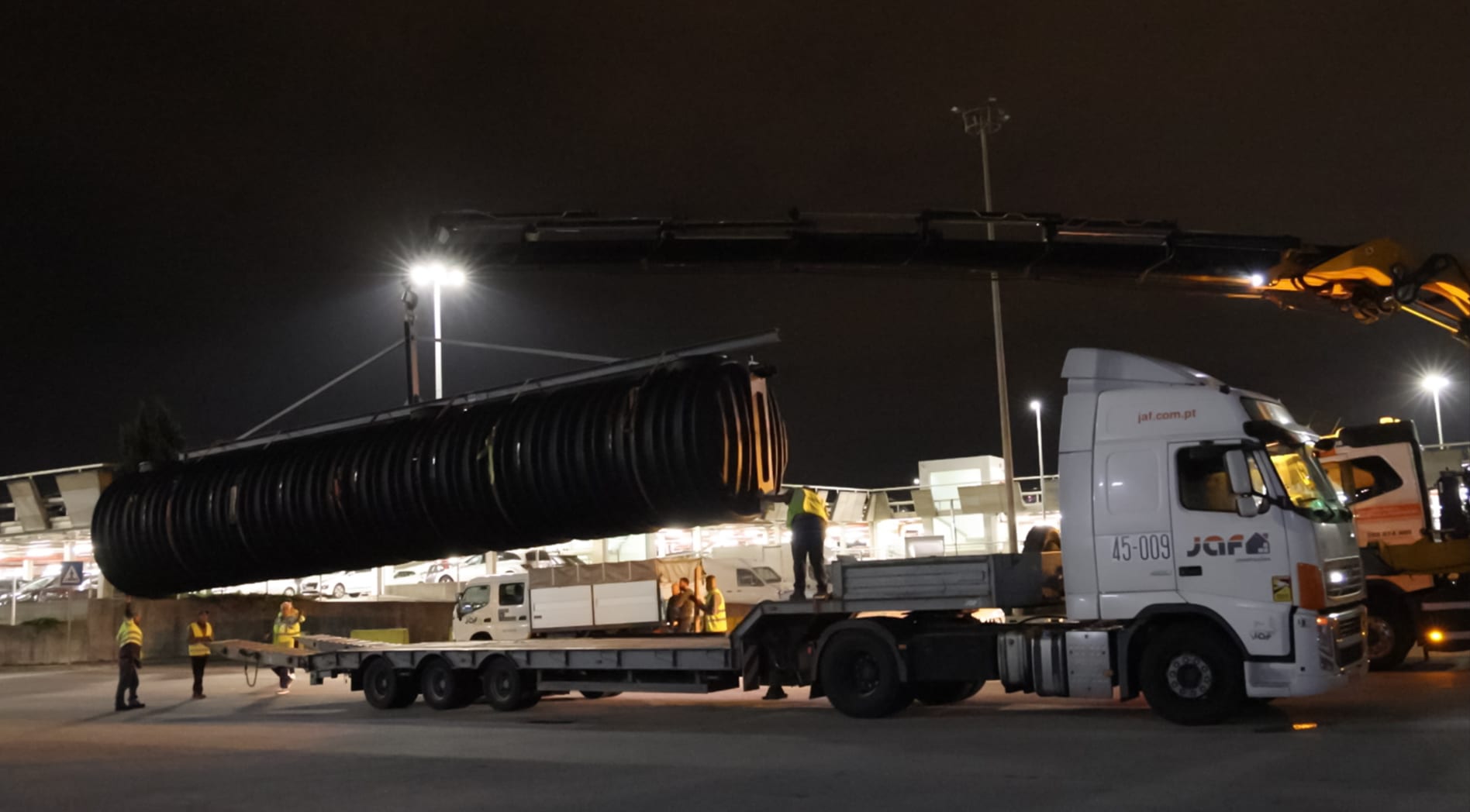 Transporte noturno de conduta de drenagem em obra
