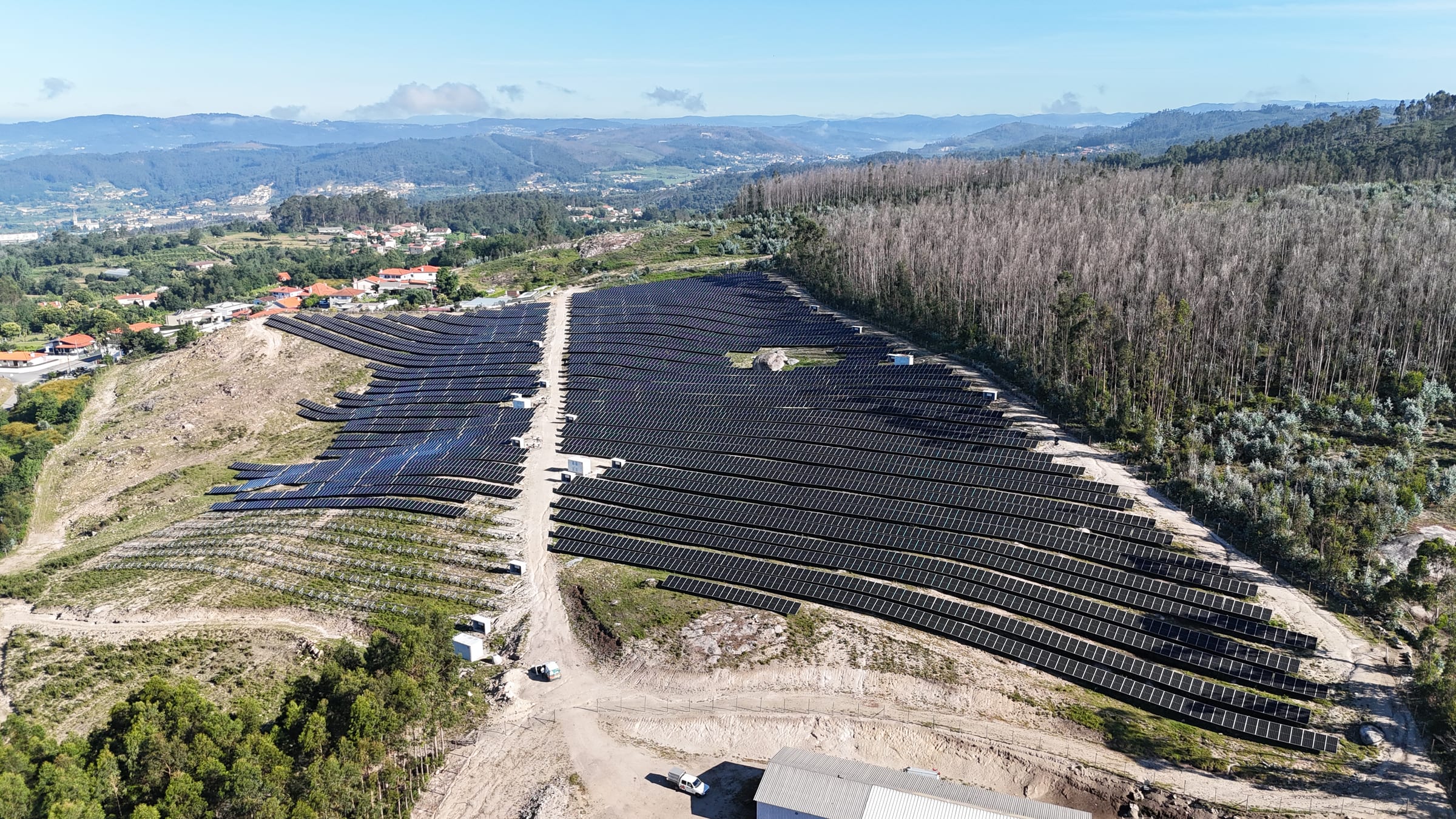 Campo fotovoltaico do Parque Solar Bela Vista sobre o vale, ao fundo uma povoação