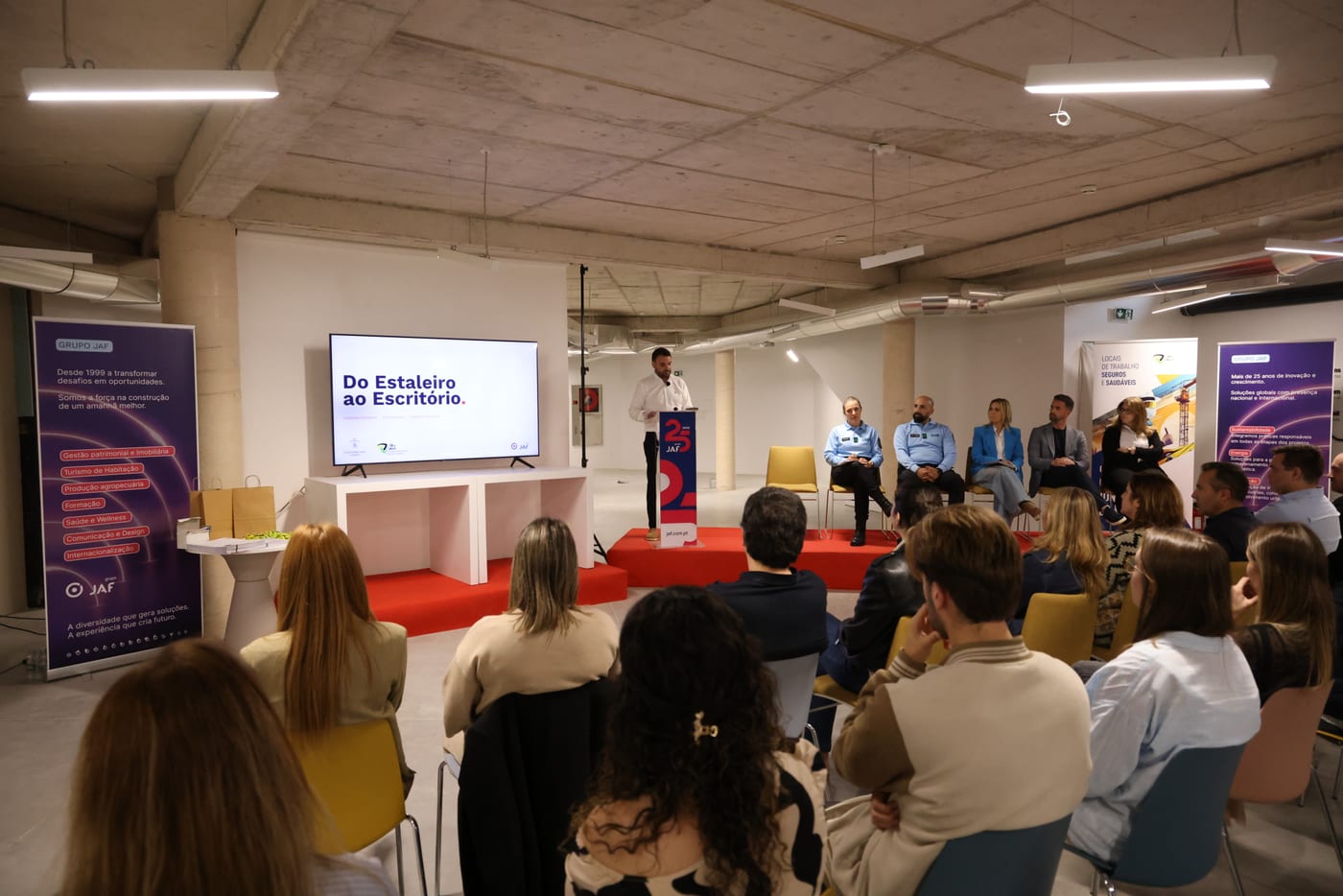 Plateia de colaboradores a assistir à apresentação, com o ecrã a mostrar o mote Do Estaleiro ao Escritório